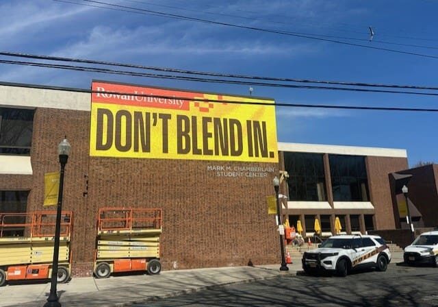 University building with "Don't Blend In" banner.