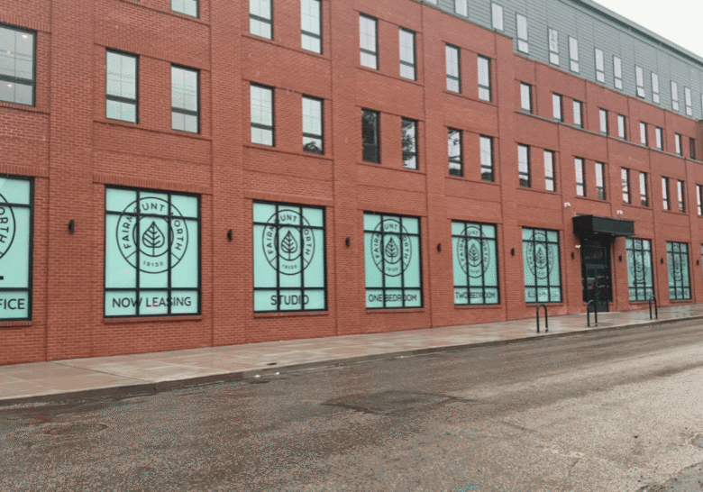 Red brick building with windows covered by black and white art and a person walking outside.